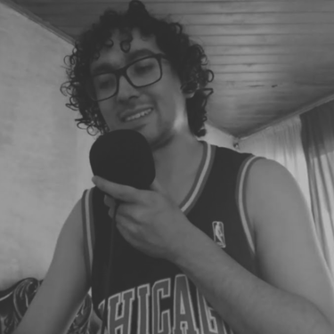 Hombre con gafas y camiseta deportiva hablando frente a un micrófono.