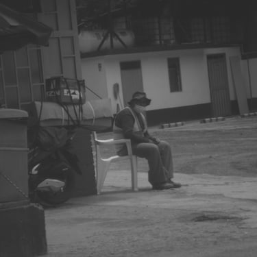 Hombre sentado en silla blanca junto a una moto cargada en la calle.