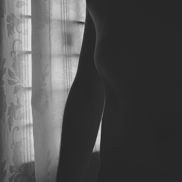 An artistic black-and-white silhouette of a torso against a curtain.