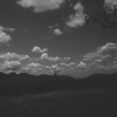 Paisaje oscuro, nubes dispersas, lomas lejanas, blanco y negro granulado.