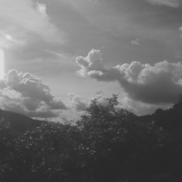 Cielo dramático con nubes sobre colinas, blanco y negro granulado.