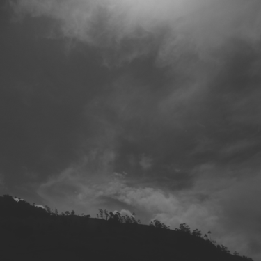 Paisaje de montaña silueteada bajo un cielo nublado y oscuro, B&N.