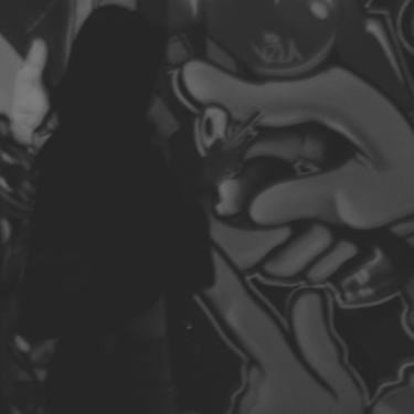 Silueta borrosa frente a un mural de grafiti, tono oscuro y monocromático.