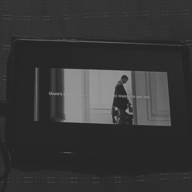 Audífonos y pantalla con cita de Bukowski, atmósfera oscura en blanco y negro.