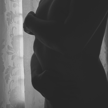 Artistic photograph of a man hugging himself in front of a sheer curtain.