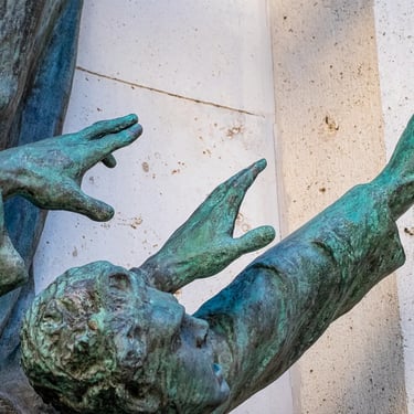 Composition of multiple students’ bronze hands extending outward in unison from the relief.