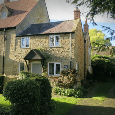 a photo of Campion Cottage, a small stone cottage in the sunshine with a lawned garden in the front