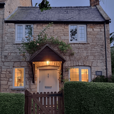 a photo of Campion Cottage, a small stone cottage at twilight with a lawned garden in the front