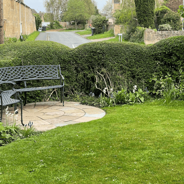 a photo of a lawn backed with hedging. There is a curved metal bench and a road visible in the distance