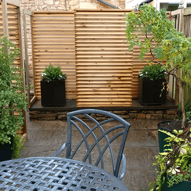 a photo of a patio garden with metal tables and chairs, plants and fencing to the rear