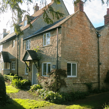 a photo of Campion Cottage, a small stone cottage in the sunshine with a lawned garden in the front