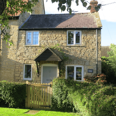 a photo of Campion Cottage, a small stone cottage in the sunshine with a lawned garden in the front
