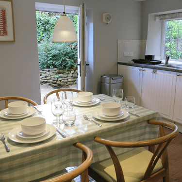 a photo of the kitchen at Campion Cottage with a table set for dinner and kitchen units and kitchen door beyond