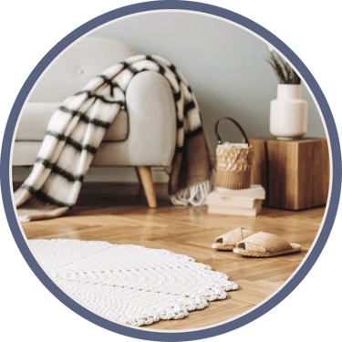A room scene features a white couch with a plaid blanket, a woven basket, plants, and slippers.
