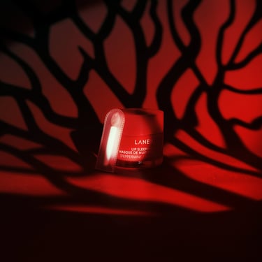 A small container of Laneige lip sleeping mask on a dark backdrop with red tree branch lighting.