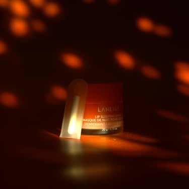 A small container of Laneige lip sleeping mask on a dark backdrop with red speckled lighting.
