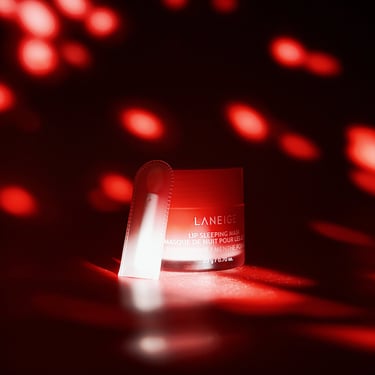 A small container of Laneige lip sleeping mask on a dark backdrop with red speckled lighting.