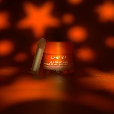 A small container of Laneige lip sleeping mask on a dark backdrop starry sky lighting.