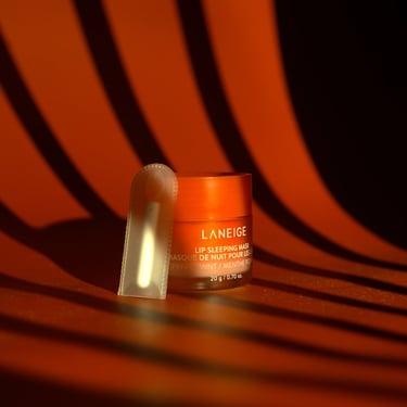 A small container of Laneige lip sleeping mask on a dark backdrop with window blind lighting.