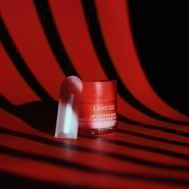 A small container of Laneige lip sleeping mask on a dark backdrop with window blind lighting.