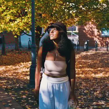 Young college black woman smiling and birdwatching underneath golden yellow autumn trees.