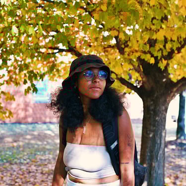 Young college black woman birdwatching underneath golden yellow autumn trees.