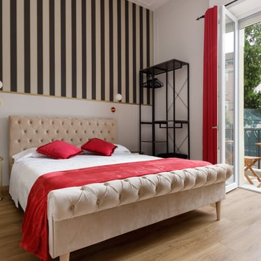 Vista ampia della camera tripla deluxe con balcone, letto matrimoniale e decorazioni rosse – Domus 44 Rooms Verona