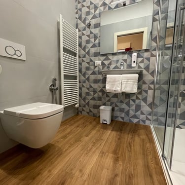 Bagno moderno della Camera Tripla Deluxe con balcone a Verona, con pavimento effetto legno, sanitari sospesi e ampia doccia i