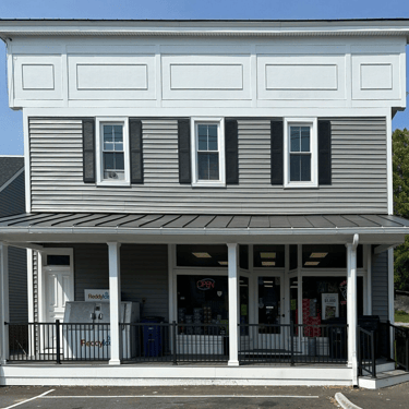 Exterior of Round Hill Market, a two-story building with gray siding, black shutters, porch, and an "Open" sign.