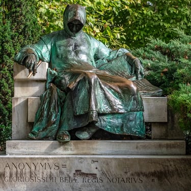 Frontal view of the entire Anonymous statue, cloaked chronicler in a stone seat.