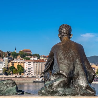 View from behind Attila József statue with Danube River and Budapest skyline beyond.