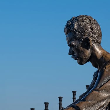 Side portrait of Attila József statue against open sky, suggesting solitude and sorrow.