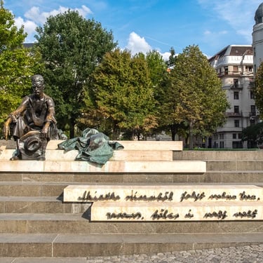 Full statue of Attila József on riverside steps with engraved verse from “At the Danube.”