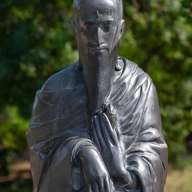 Upper body with head and hands framed by trees and greenery.