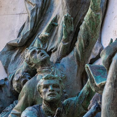 Bronze hands of three students extend outward together from the relief.