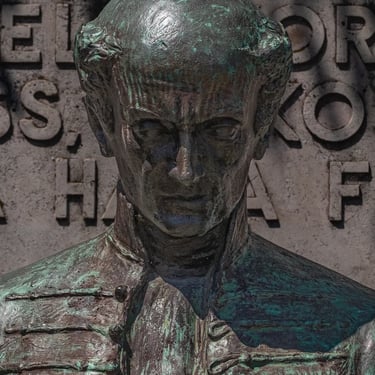 Front view of Ferenc Kölcsey's statue against a stone background.