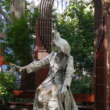Complete Liszt statue framed by an ornate arch and trees, blending tribute and setting.