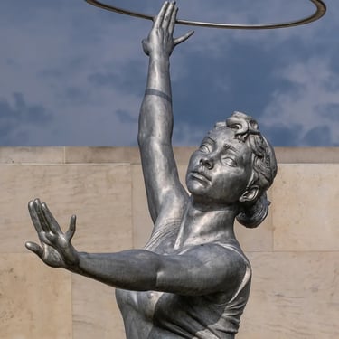 Upper body of first gymnast girl, bronze hoop lifted high in graceful athletic pose.