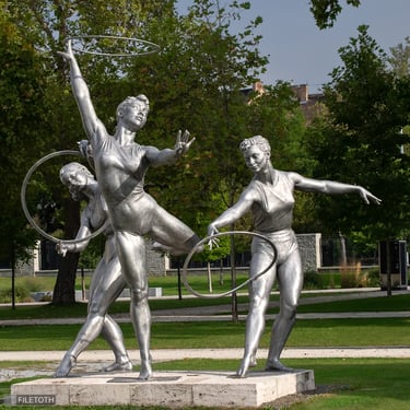 Front view of three bronze gymnast girls with hoops, united in rhythmic movement.