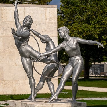 Side view of three gymnast girls with hoops, synchronized poses and flowing lines.