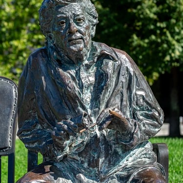 Front view of Hilda Gobbi statue with empty chair beside her, inviting an unseen partner.