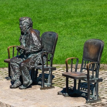 Side view of seated Hilda Gobbi statue with an empty chair evoking calm contemplation.