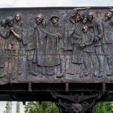 Memorial wagon with three leaping figures set among larger groups of deported people.