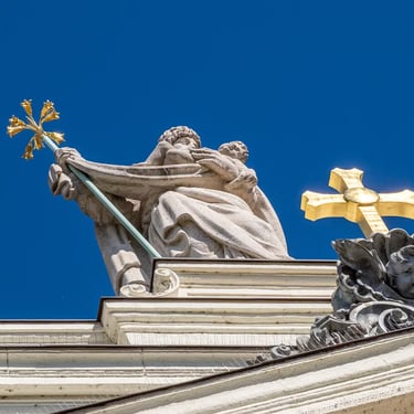 Saint Joseph statue with a cross, on top of the church, set against a bright sky background.