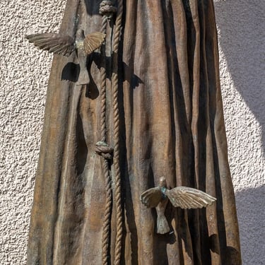 Lower part of statue with clustered birds on robe, evoking harmony with nature.