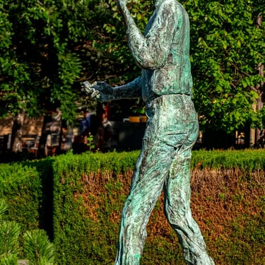 Full Steve Jobs statue stepping forward, surrounded by green trees in the background.