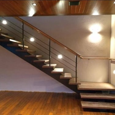 Escada com viga central, degraus de madeira e guarda-corpo de metal com corrimão de madeira, em ambiente com piso e teto tamb