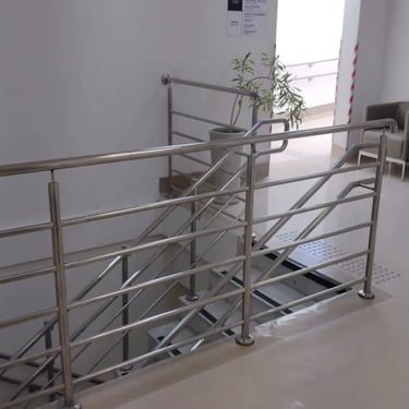 Guarda-corpo de aço inoxidável com barras horizontais protegendo a abertura de uma escada em um ambiente interno de um edifíc