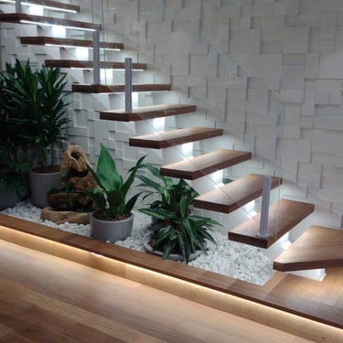 Vista ampla da escada flutuante com degraus de madeira iluminados e uma parede com revestimento cimentício 3D em relevo ao fu