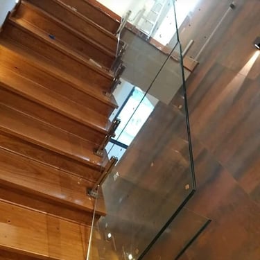 Vista superior de uma escada com degraus de madeira e guarda-corpo de vidro fixado com suportes de aço inox na lateral dos de